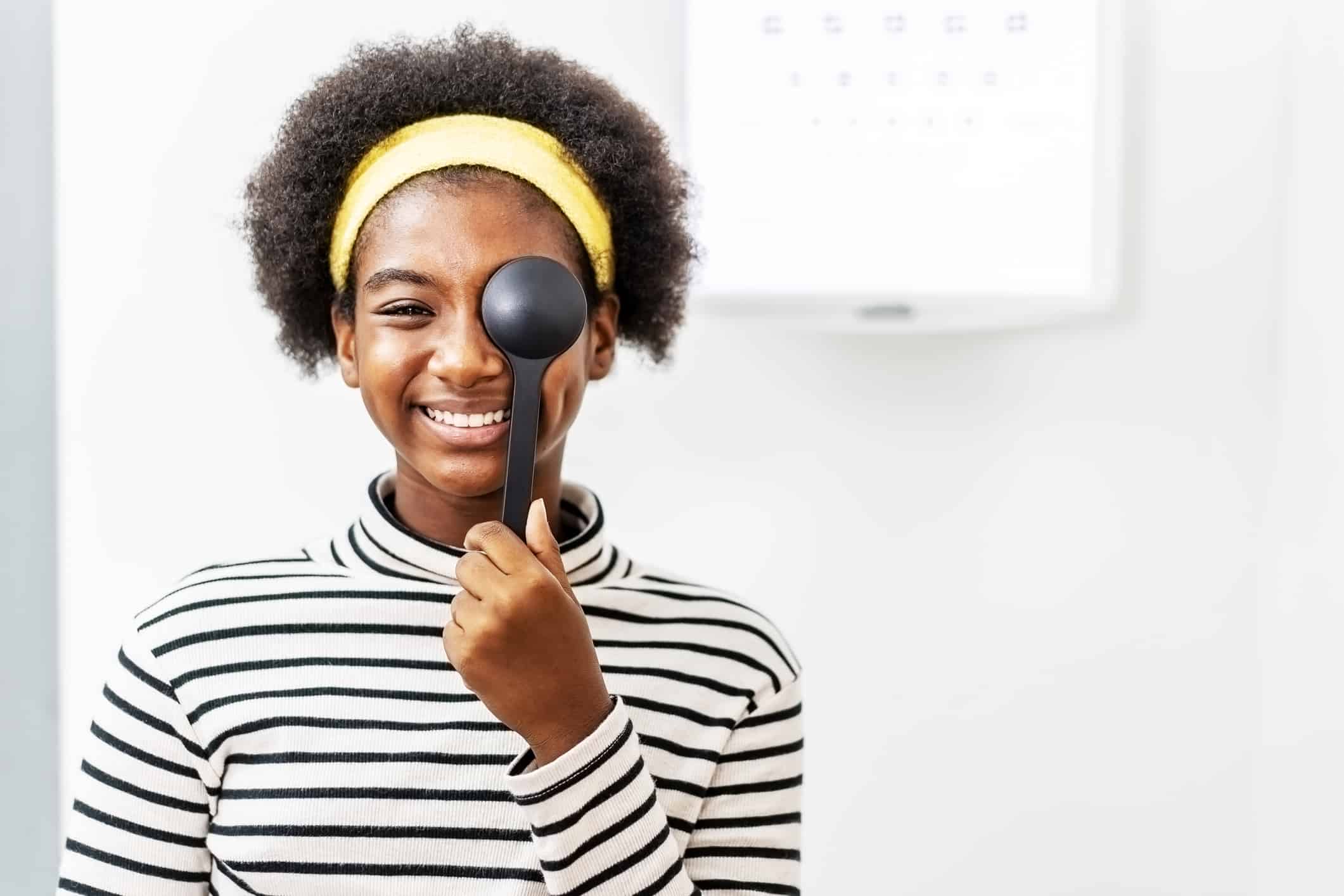 Smiling young woman eye test in ophthalmological clinics, holding occluder and looking at chart